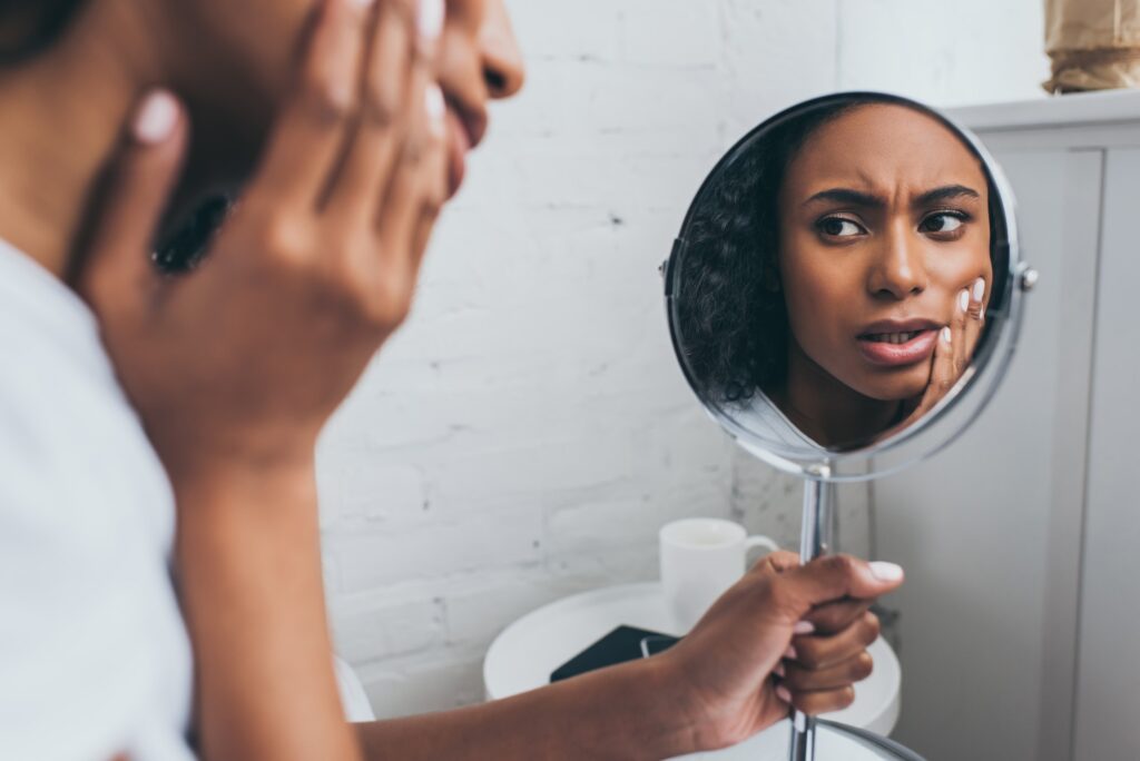 pretty african american woman looking at mirror while suffering from tooth pain